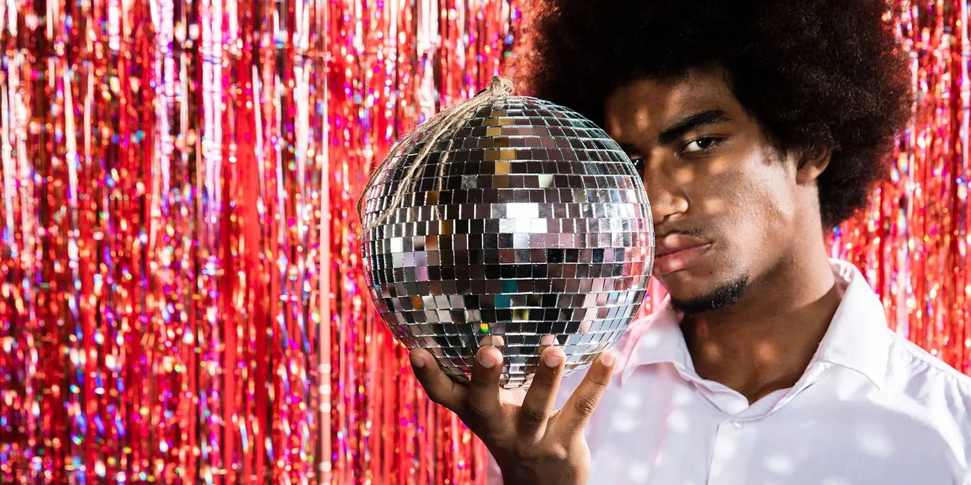Man holding a disco ball in front of red tinsel backdrop